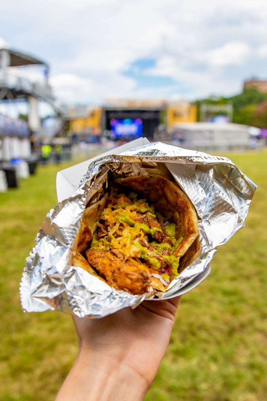 Hand holding a gyro in green grass near OMF festival stage